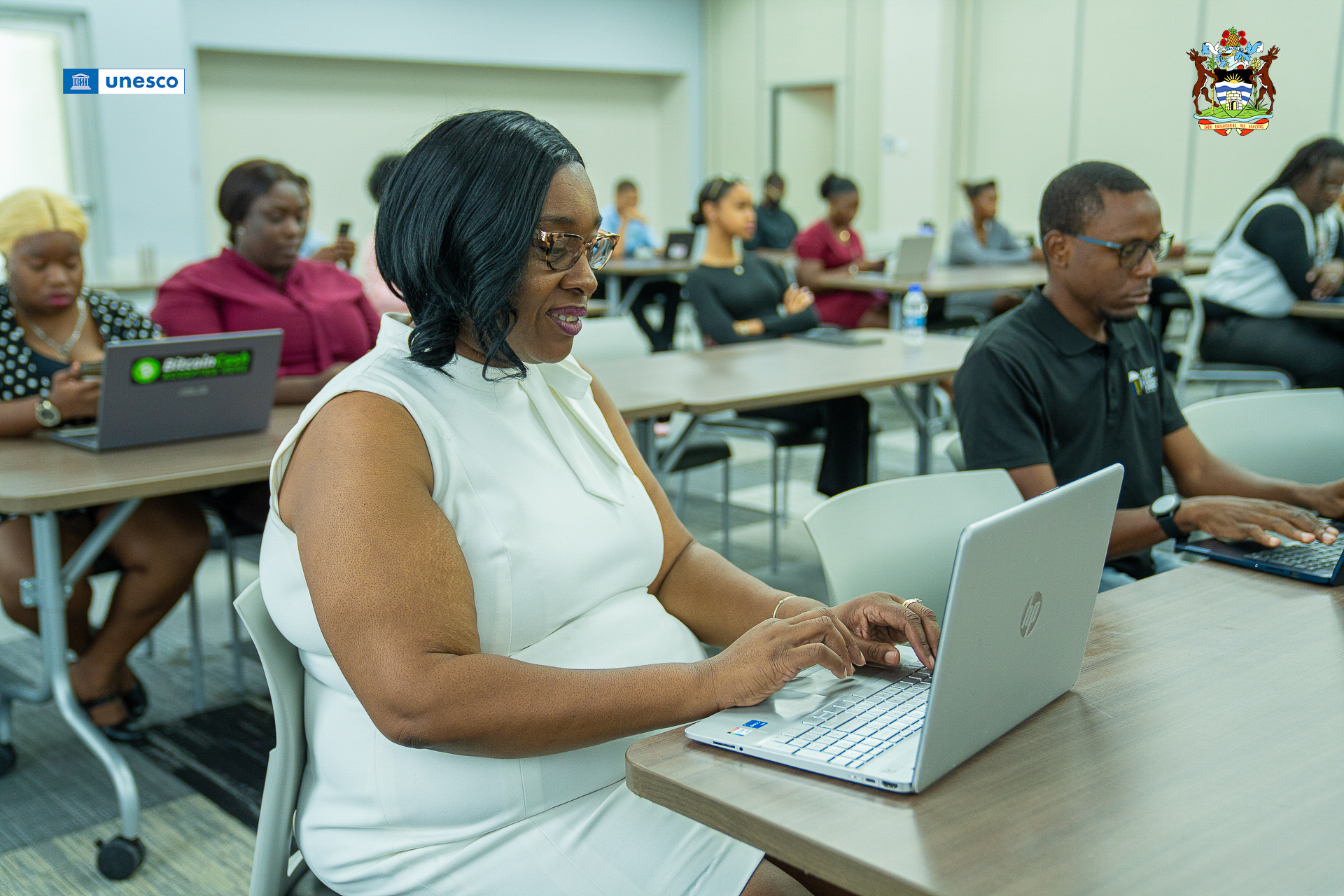 Principal of the Antigua State College, Dr. N’Agele Buffonge attends the opening ceremony. She is seated with a grey laptop in front of her.