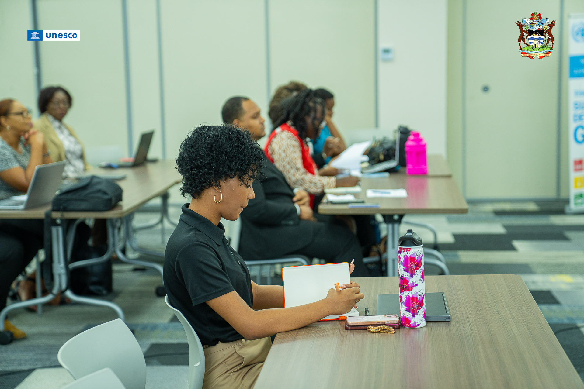 Ms. Jhaka Wooding, a youth journalist from the Cayman Islands, sits at the table writing into a book.